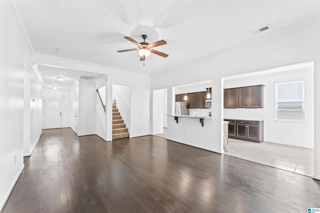 unfurnished living room featuring ceiling fan, light wood-type flooring, crown molding, stairs, and visible vents
