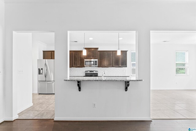 kitchen with stainless steel appliances, decorative backsplash, a kitchen breakfast bar, light stone counters, and dark brown cabinets