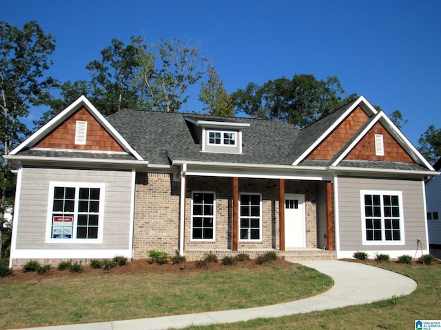 craftsman inspired home featuring brick siding, a porch, a shingled roof, and a front lawn