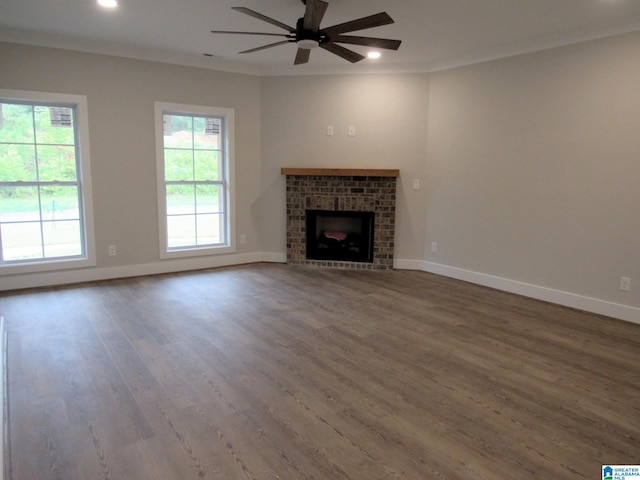 unfurnished living room featuring a ceiling fan, wood finished floors, crown molding, baseboards, and a brick fireplace
