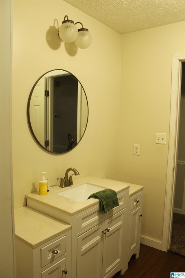 bathroom with baseboards, vanity, wood finished floors, and a textured ceiling
