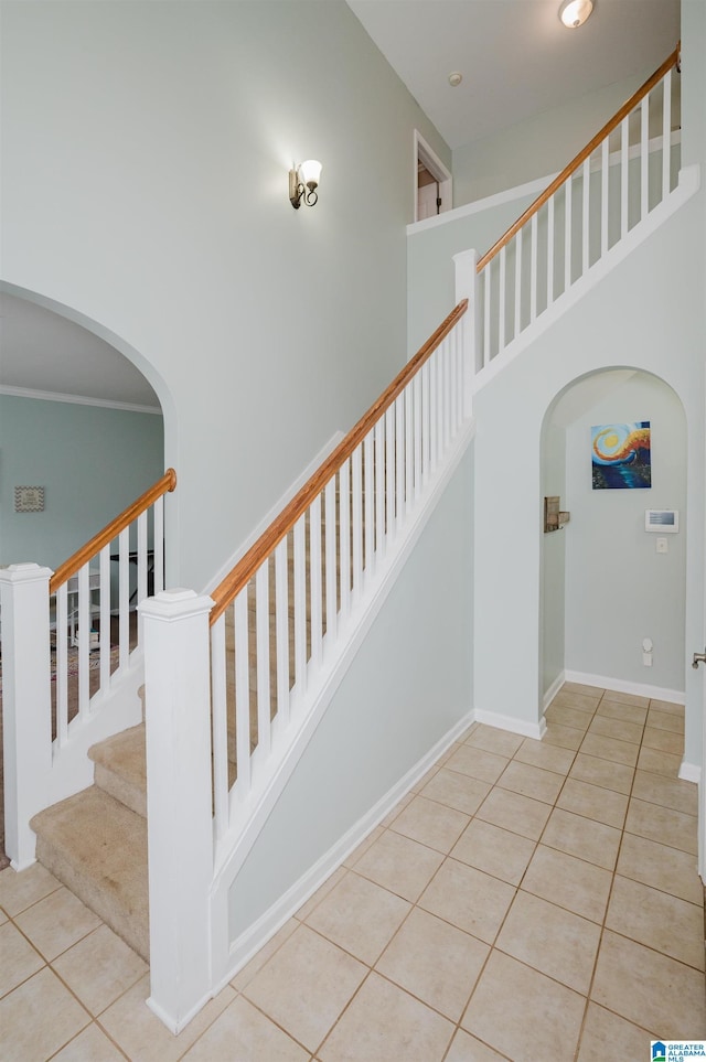 staircase with tile patterned floors, arched walkways, a high ceiling, and baseboards