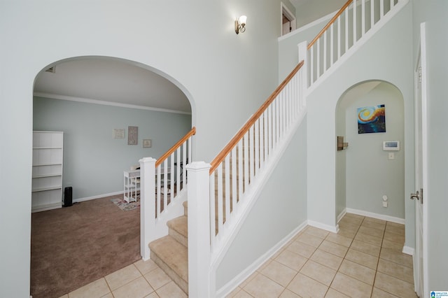 staircase with arched walkways, ornamental molding, tile patterned flooring, carpet floors, and a high ceiling