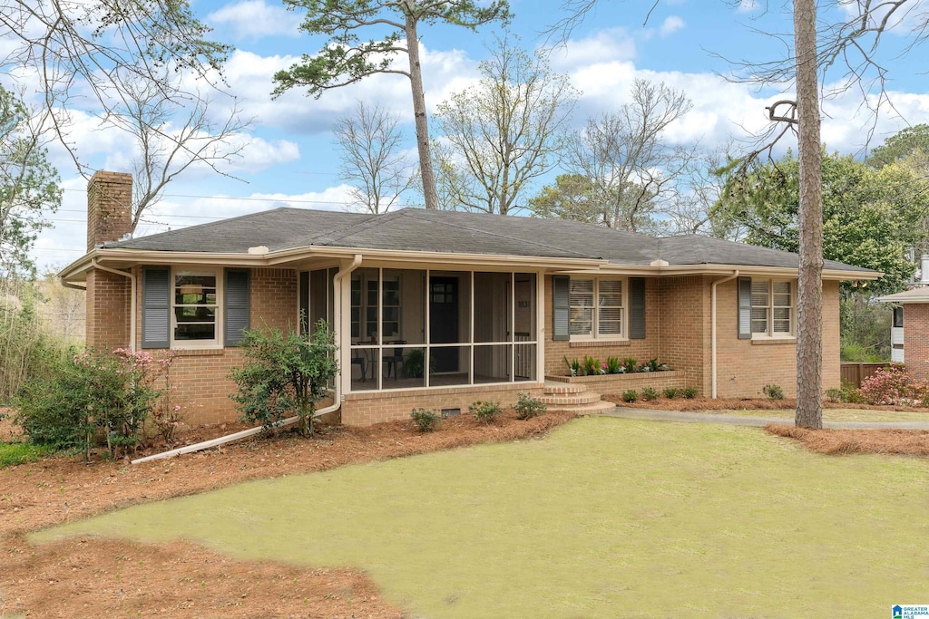 view of front of house featuring brick siding, a sunroom, a front lawn, and a chimney