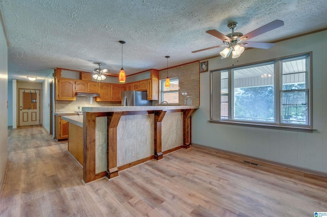 kitchen with a peninsula, light wood finished floors, a ceiling fan, and freestanding refrigerator