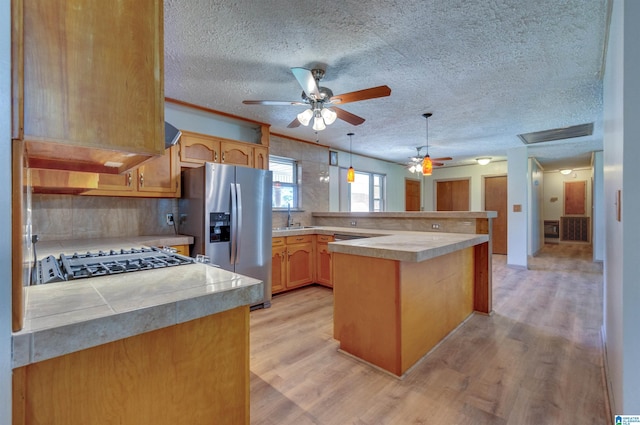 kitchen with a ceiling fan, a peninsula, stainless steel fridge with ice dispenser, and light countertops