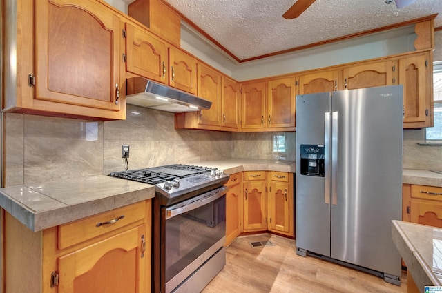 kitchen featuring a textured ceiling, light wood-style flooring, light countertops, under cabinet range hood, and appliances with stainless steel finishes
