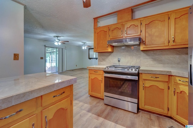 kitchen with under cabinet range hood, light wood-style flooring, stainless steel gas range, and a ceiling fan