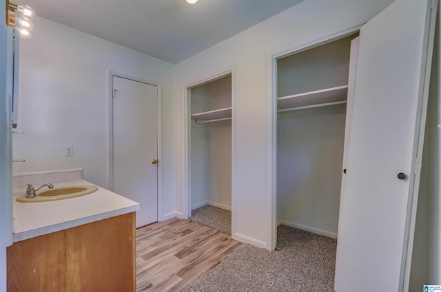 bathroom featuring vanity, wood finished floors, baseboards, a textured ceiling, and a walk in closet