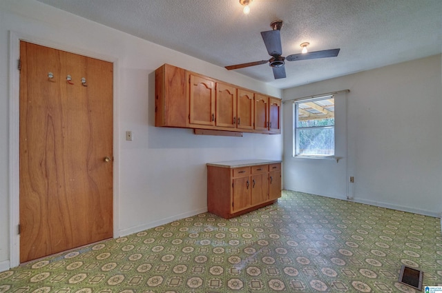 interior space featuring visible vents, baseboards, ceiling fan, light floors, and brown cabinetry