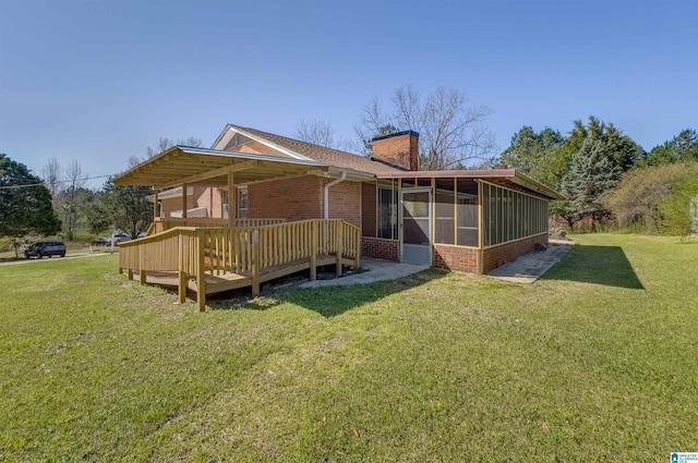 rear view of house featuring a yard, a sunroom, a wooden deck, brick siding, and a chimney