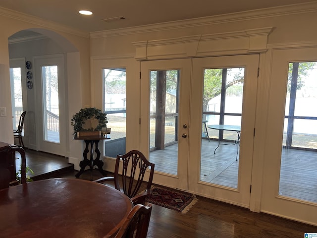 dining area featuring dark wood finished floors, ornamental molding, french doors, and arched walkways