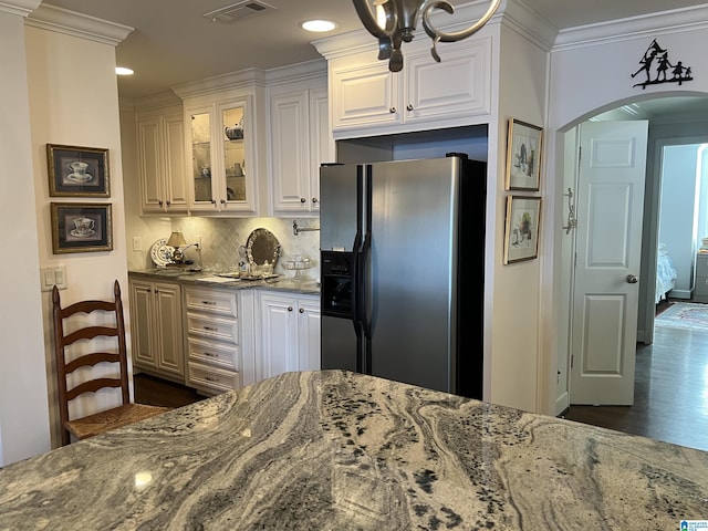 kitchen with visible vents, crown molding, fridge with ice dispenser, dark stone countertops, and arched walkways