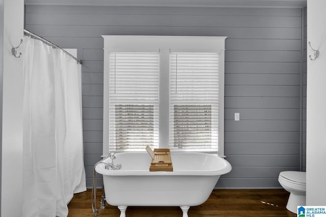 full bathroom featuring toilet, wood finished floors, wood walls, and a freestanding bath