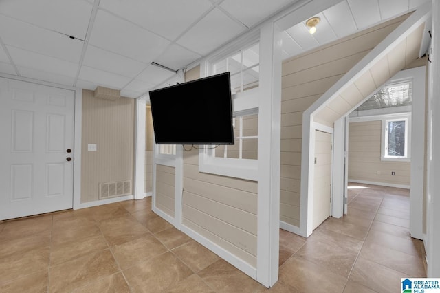 corridor with visible vents, a paneled ceiling, and wood walls
