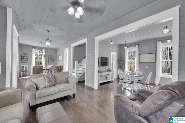 living area with stairway, ceiling fan with notable chandelier, wood ceiling, and dark wood-style flooring