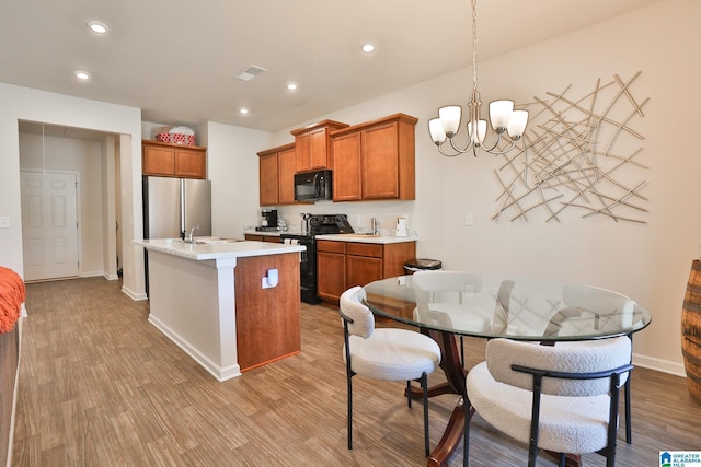 kitchen with light countertops, wood finished floors, brown cabinets, a center island with sink, and black appliances