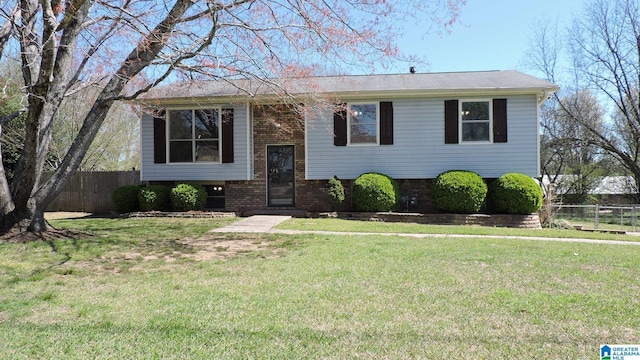 raised ranch featuring brick siding, fence, and a front yard