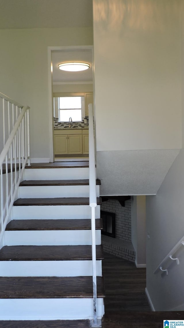 staircase with a brick fireplace, baseboards, and wood finished floors