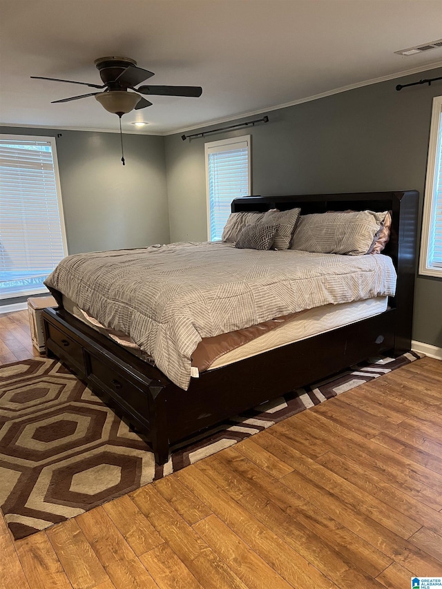bedroom featuring crown molding, a ceiling fan, wood finished floors, baseboards, and visible vents