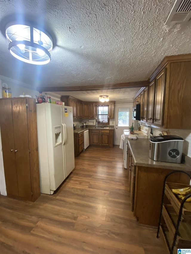 kitchen with a sink, a textured ceiling, white appliances, visible vents, and dark wood-type flooring