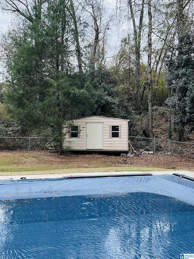 view of swimming pool featuring an outbuilding, fence, a covered pool, and a shed