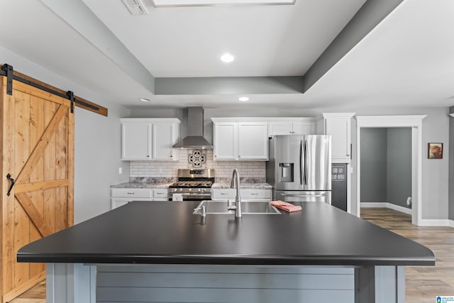 kitchen with a sink, white cabinetry, a barn door, wall chimney exhaust hood, and stainless steel appliances