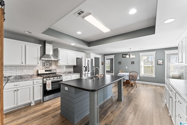 kitchen with wall chimney exhaust hood, a tray ceiling, a sink, and stainless steel appliances