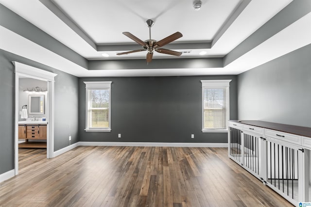 spare room featuring hardwood / wood-style floors, a raised ceiling, baseboards, and ceiling fan