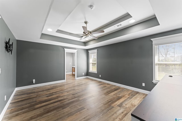 empty room featuring baseboards, a tray ceiling, wood finished floors, and ceiling fan