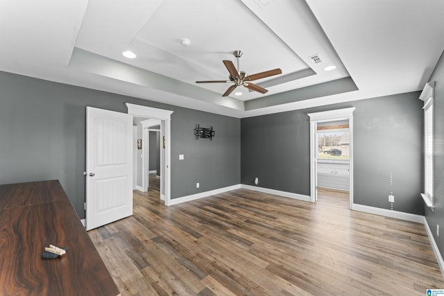 unfurnished bedroom featuring a tray ceiling, wood finished floors, baseboards, visible vents, and ceiling fan