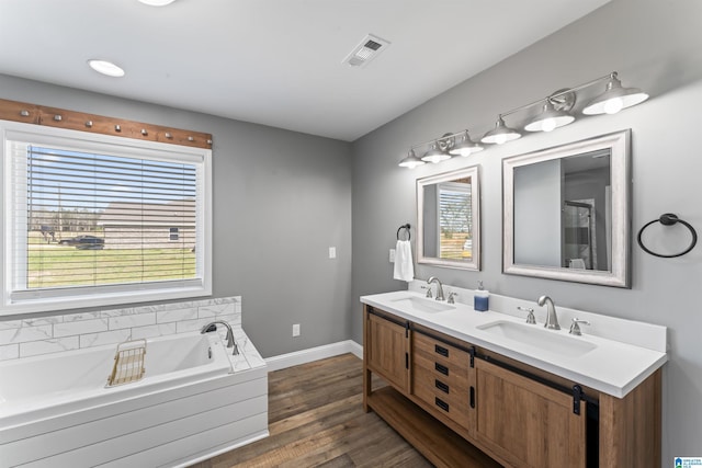 bathroom with wood finished floors, a sink, a garden tub, and visible vents