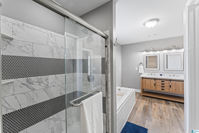 bathroom featuring double vanity, wood finished floors, a sink, a stall shower, and a garden tub