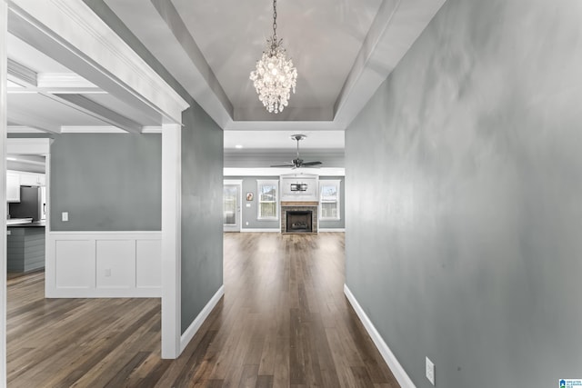 corridor with a decorative wall, a chandelier, a raised ceiling, dark wood finished floors, and wainscoting
