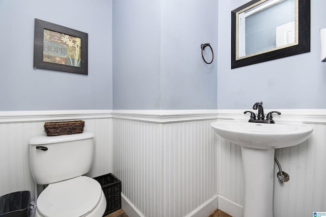 half bathroom featuring a sink, toilet, and wainscoting
