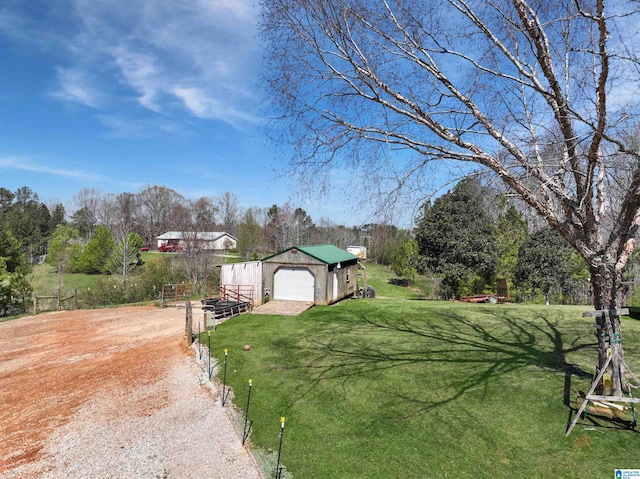 view of yard with driveway, a detached garage, fence, and an outdoor structure