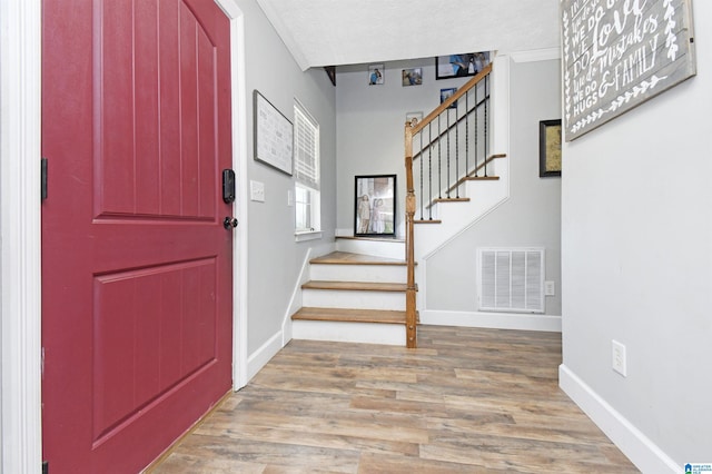 foyer with stairs, visible vents, wood finished floors, and baseboards