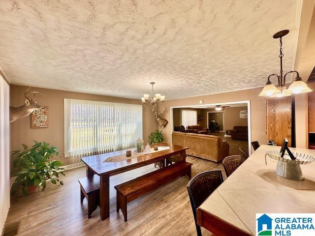 dining space with an inviting chandelier, a textured ceiling, baseboards, and wood finished floors