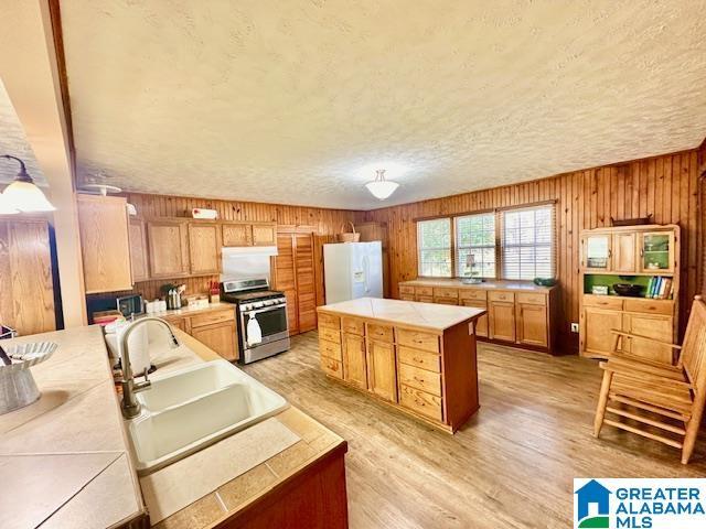 kitchen featuring tile counters, white fridge with ice dispenser, gas stove, a sink, and light wood-type flooring