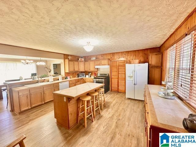 kitchen featuring a sink, light wood finished floors, under cabinet range hood, stainless steel appliances, and tile countertops