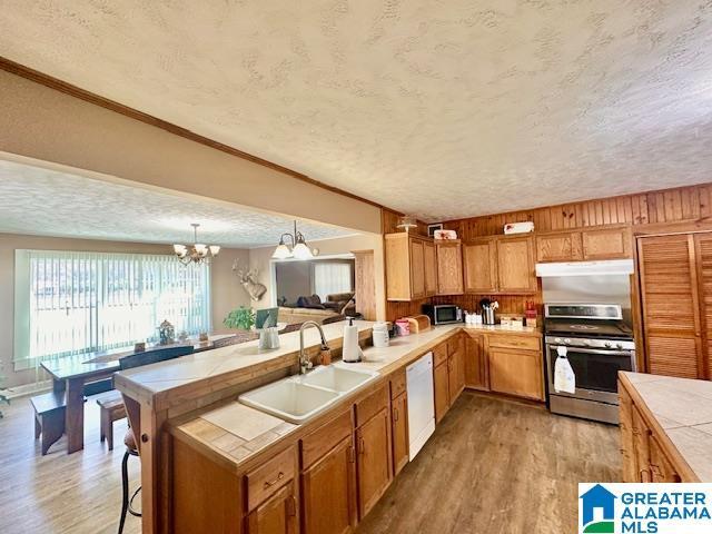 kitchen featuring a notable chandelier, a sink, tile counters, stainless steel range with electric stovetop, and white dishwasher