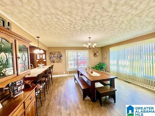 dining room with a textured ceiling, visible vents, baseboards, wood finished floors, and an inviting chandelier