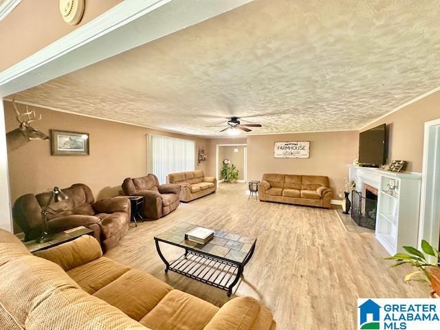 living room featuring ornamental molding, a fireplace with flush hearth, a textured ceiling, ceiling fan, and wood finished floors