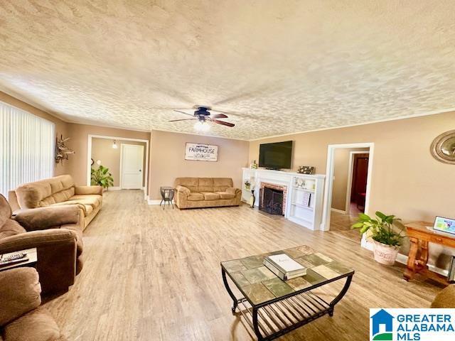 living area with a ceiling fan, a fireplace, wood finished floors, a textured ceiling, and baseboards