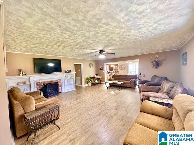 living area with a brick fireplace, a textured ceiling, wood finished floors, and a ceiling fan