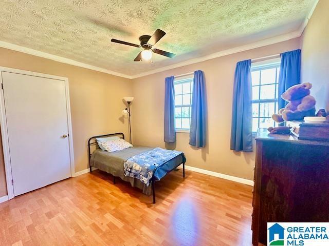 bedroom with a textured ceiling, light wood-style flooring, ceiling fan, and crown molding