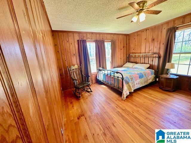 bedroom with crown molding, wooden walls, light wood finished floors, and a textured ceiling