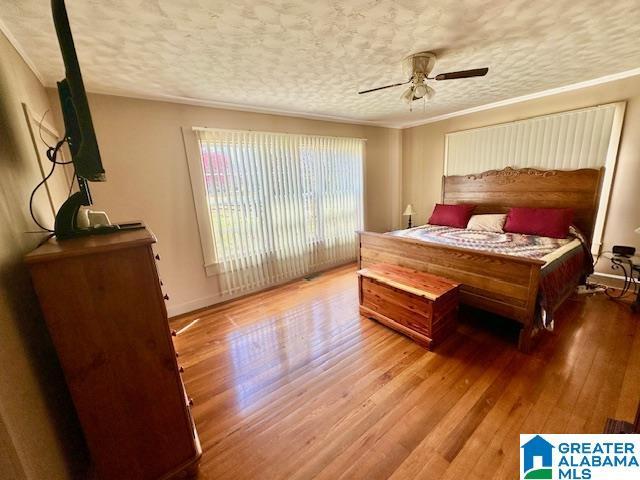 bedroom with a ceiling fan, wood finished floors, a textured ceiling, baseboards, and ornamental molding