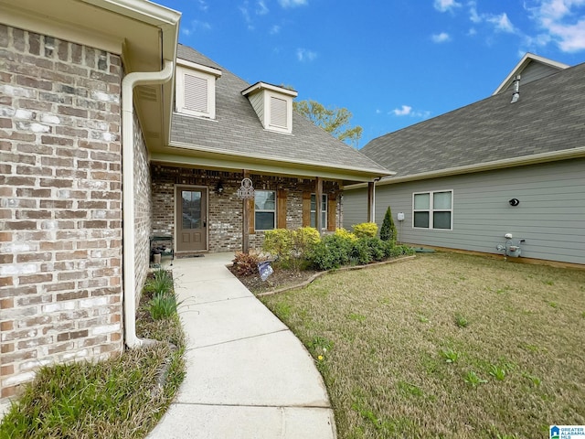 property entrance featuring roof with shingles, brick siding, and a lawn