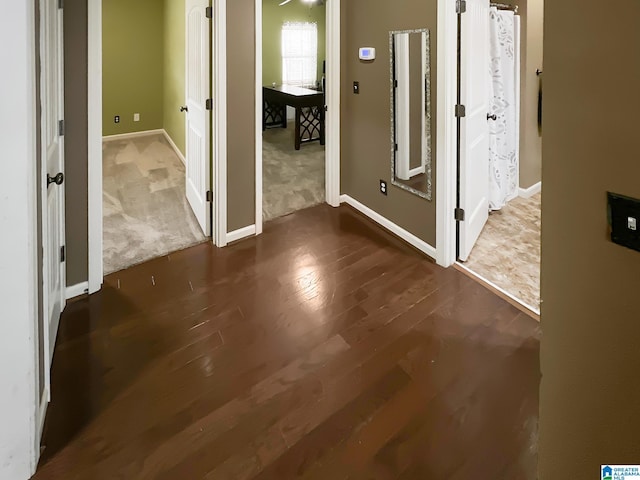corridor featuring dark wood-type flooring and baseboards